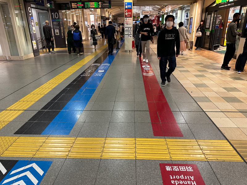 People walking through a wide corridor.  Yellow, red, blue and black lines on ground indicate pathways to destinations. 