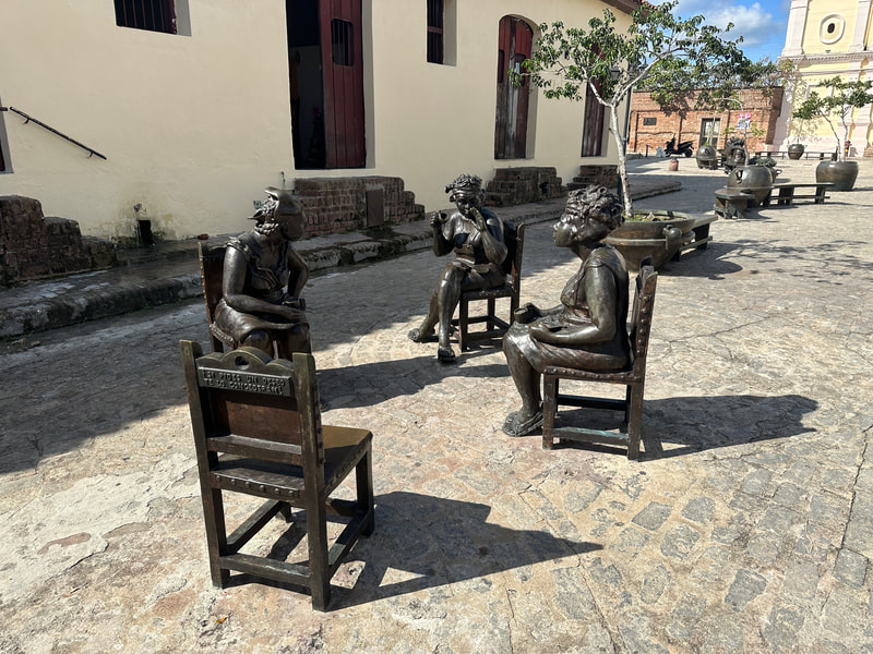Four stone statues seated on chairs. 