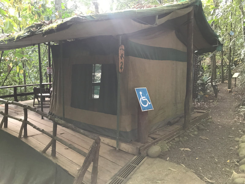 Safari tent in forest with ramp and wheelchair accessible sign in front.  