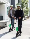 Two people stand upright on scooters.