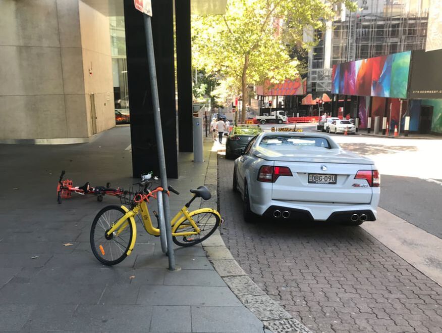 Two bicycles laying on sidewalk beside parked car on street.