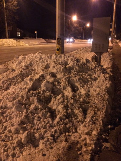 Large pile of snow in front of traffic poll with button for pedestrian crossing.