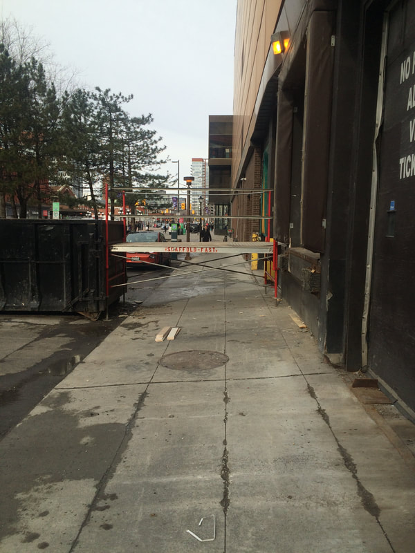 Construction walkway blocks sidewalk at hip level between building and dumpster. 