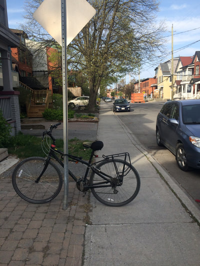 Bicycle extends across city sidewalk.  Parked car on street. 