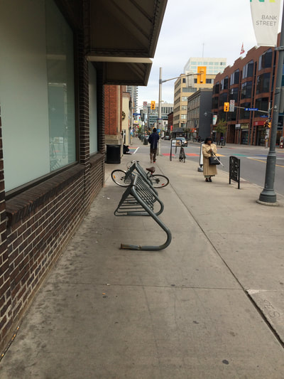 Empty bicycle rack on wide sidewalk between building and street.