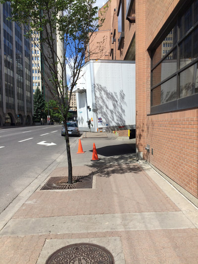 Transport truck trailer extends across sidewalk from behind building. 