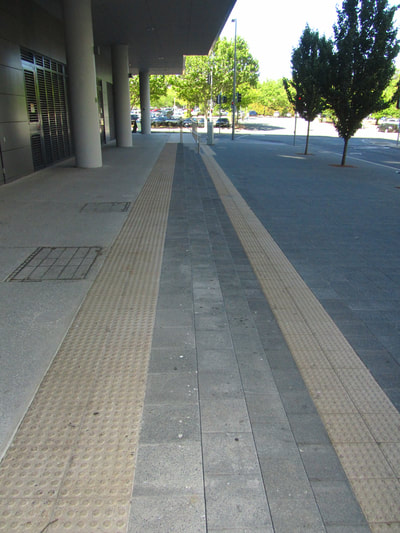 Sidewalk with row of textured dome indicating steps and incline. 