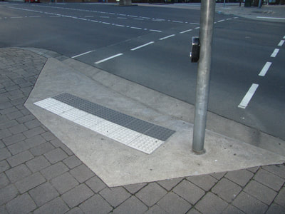Entrance to a cross walk with textured curb and crossing signal button on post.