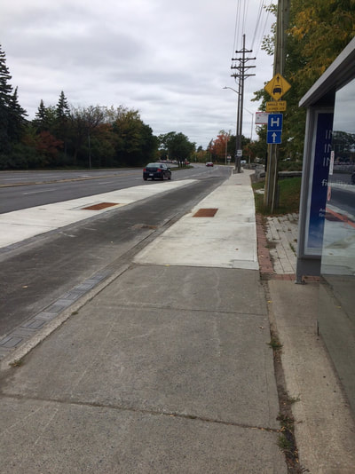 Bus shelter next to sidewalk with bike lane between two sidewalk sections.