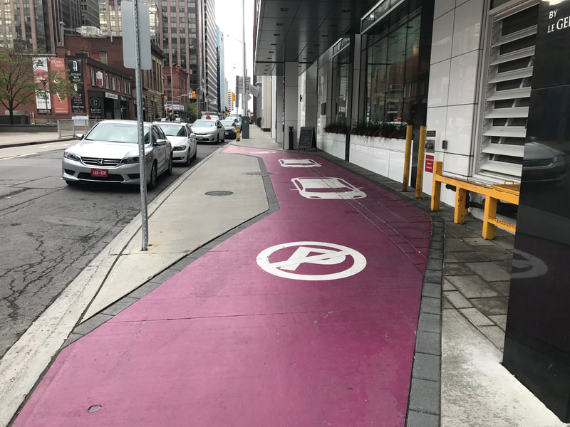 View down city sidewalk.  Purple paint on sidewalk depicts driveway and parking.
