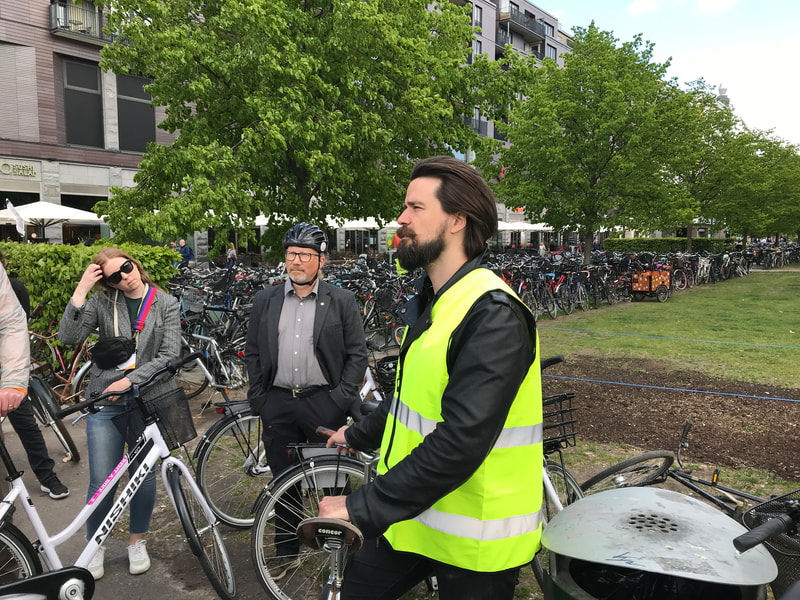 Man in reflective vest speaks to group of cyclists. 
