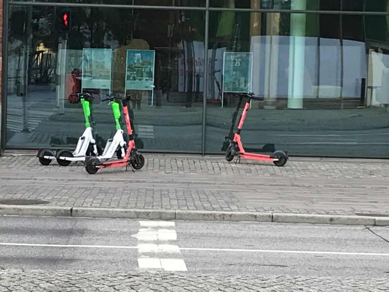 Several scooters parked on sidewalk between road and building. 