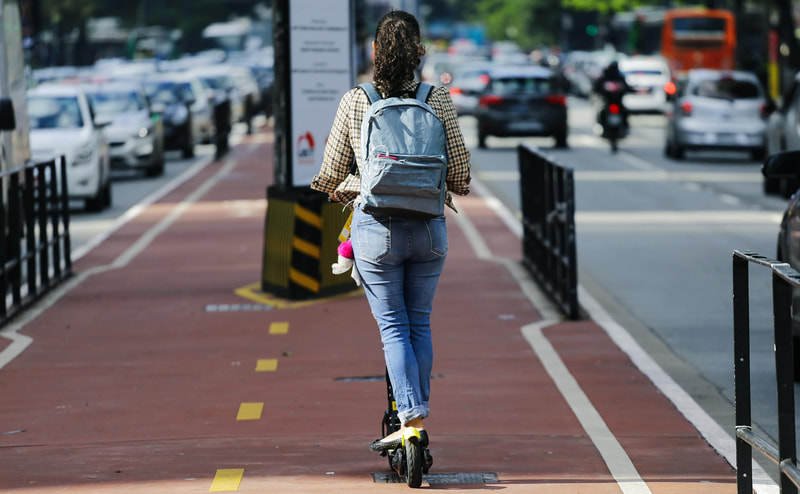 Women standing on scooter riding away from view on two laned cycle path.